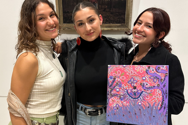 Picture of 3 NDGNS girls smiling for a picture, with the girl on the right holding up a pink and purple painting